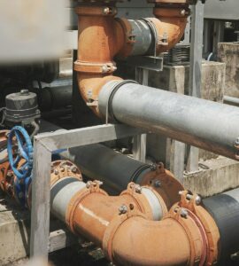 Workers install a labeled prefabricated piping assembly in a partially finished building.
