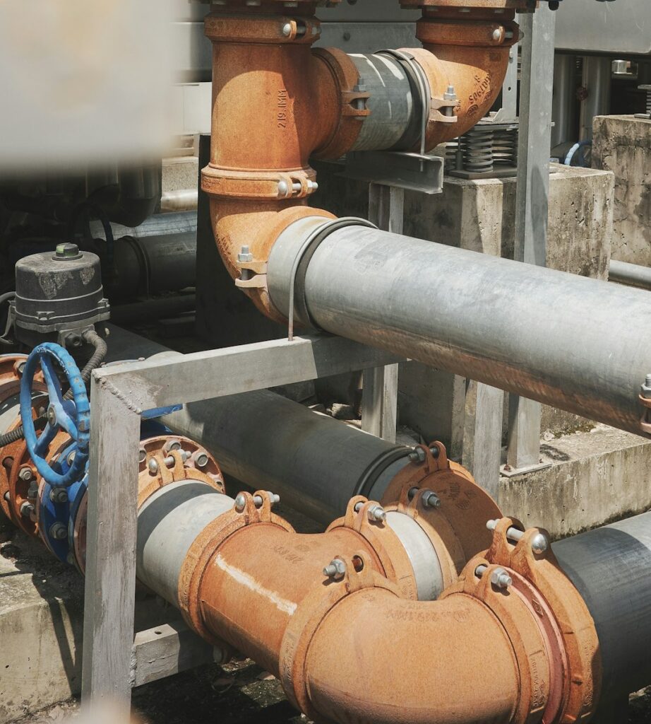 Workers install a labeled prefabricated piping assembly in a partially finished building.